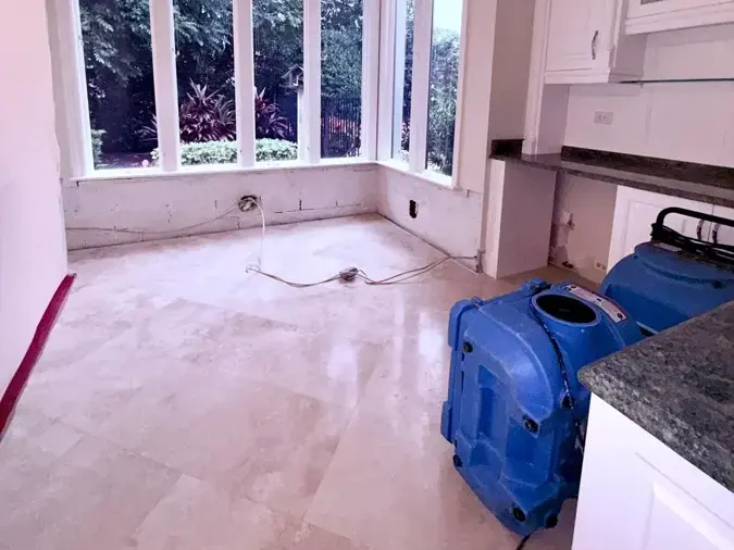 Blue drying unit beside a granite counter in a tiled room with tall windows and the baseboards pulled