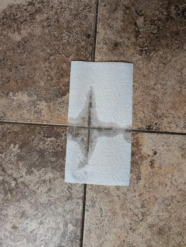 Paper towel on a tile floor showing a wet grout joint, a common slab leak sign