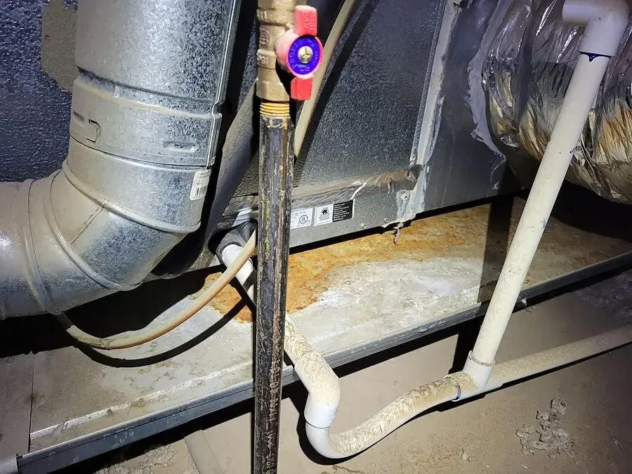 Rust-stained, wet drain pan and condensate lines under an air handler