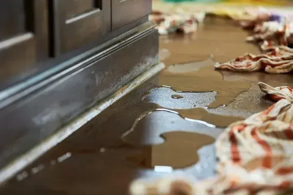 Water pooled along the base of a kitchen cabinet with towels laid down