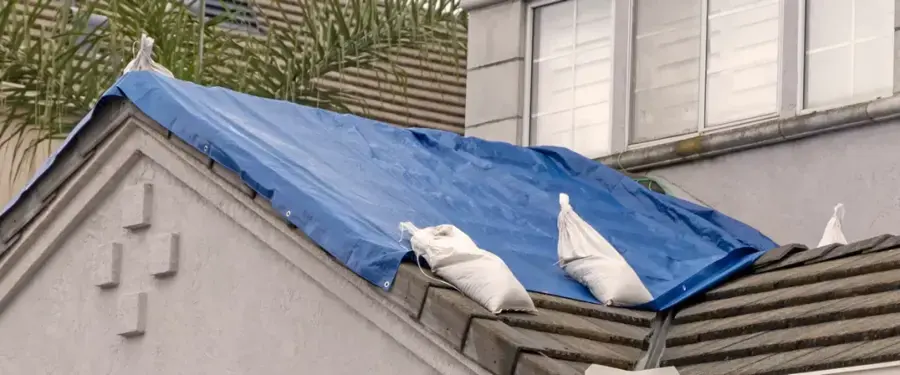 Blue tarp held down with sandbags over a storm-damaged tile roof
