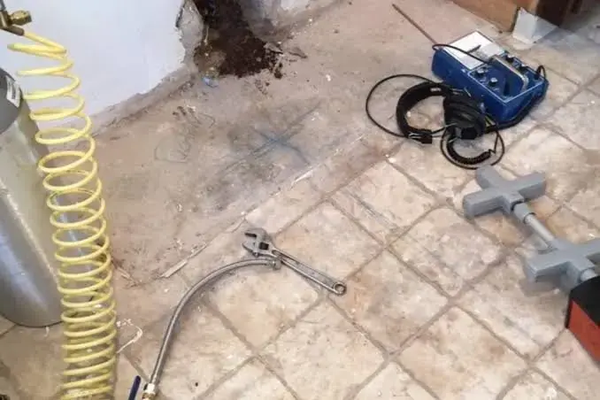 Leak detection gear beside an opened patch of tile floor where a slab leak was traced