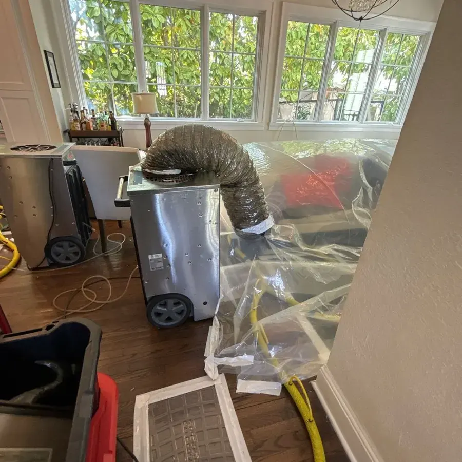 Dehumidifier ducted under plastic containment to dry a room with hardwood floors