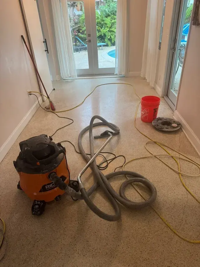 Wet vacuum, hoses and a bucket set out on a terrazzo floor to pull up standing water