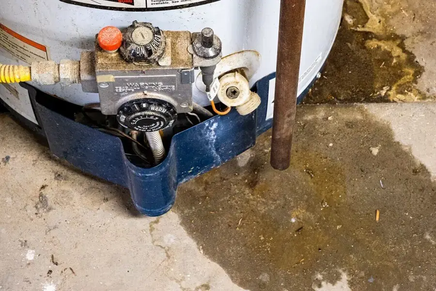 Rust and water pooled on a concrete floor at the base of a gas water heater